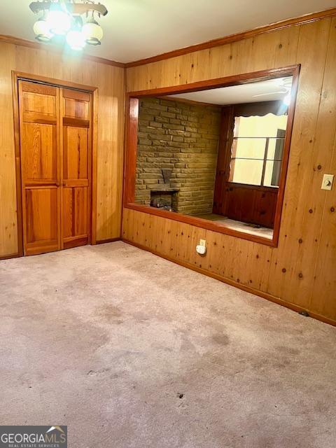 unfurnished living room with a wood stove, wood walls, and light colored carpet