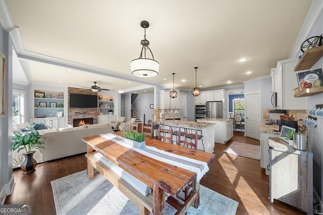 dining space featuring built in shelves, a fireplace, ornamental molding, and dark wood-type flooring