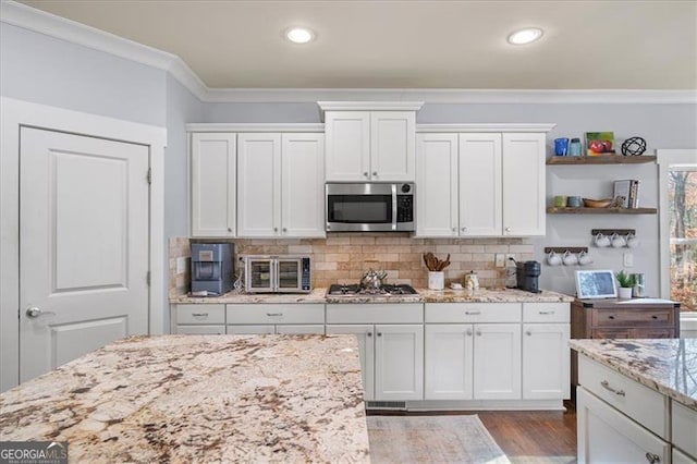 kitchen featuring crown molding, decorative backsplash, light stone counters, white cabinetry, and stainless steel appliances