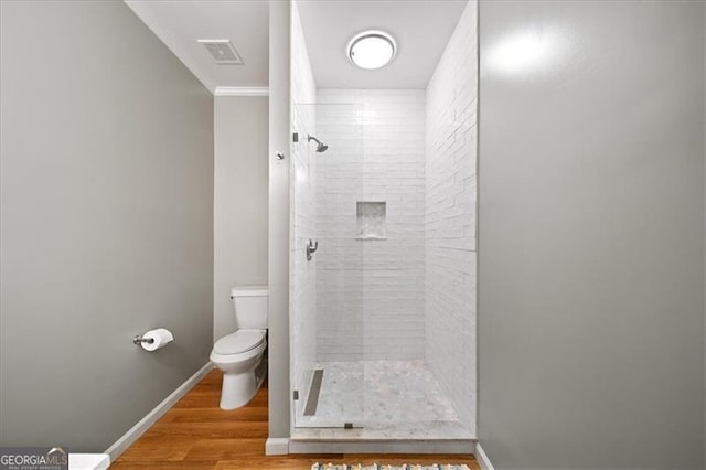 bathroom featuring a tile shower, toilet, ornamental molding, and hardwood / wood-style floors