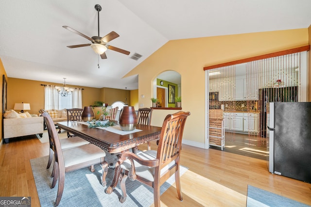 dining area featuring ceiling fan with notable chandelier, light hardwood / wood-style floors, and vaulted ceiling