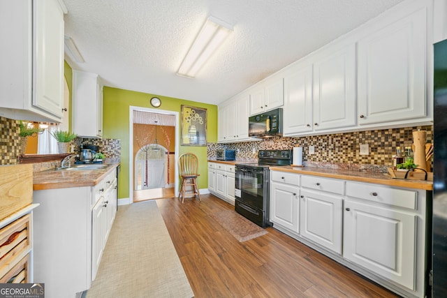 kitchen with wooden counters, black appliances, sink, light hardwood / wood-style flooring, and white cabinetry