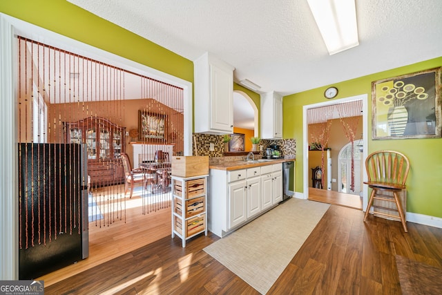 kitchen with backsplash, a textured ceiling, black dishwasher, dark hardwood / wood-style flooring, and white cabinetry