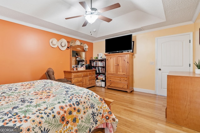 bedroom with ceiling fan, ornamental molding, a textured ceiling, a tray ceiling, and light wood-type flooring