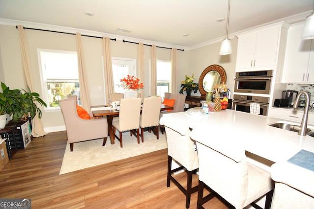 kitchen with light wood-type flooring, stainless steel double oven, sink, decorative light fixtures, and white cabinetry