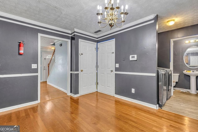 foyer entrance featuring wood finished floors, a textured ceiling, a chandelier, baseboards, and crown molding