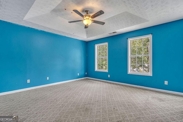 unfurnished room featuring a textured ceiling, a raised ceiling, a ceiling fan, carpet, and baseboards