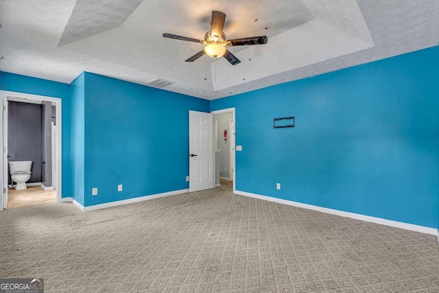 unfurnished bedroom with a textured ceiling, carpet flooring, baseboards, and a tray ceiling