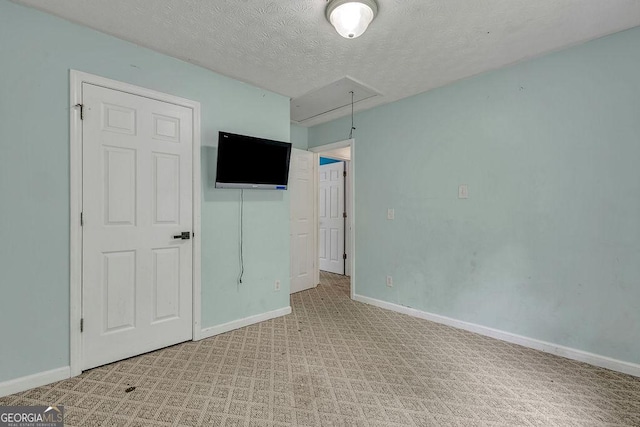 spare room with attic access, light carpet, baseboards, and a textured ceiling