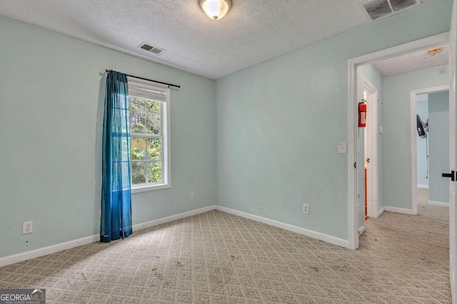 empty room featuring a textured ceiling, light colored carpet, and baseboards
