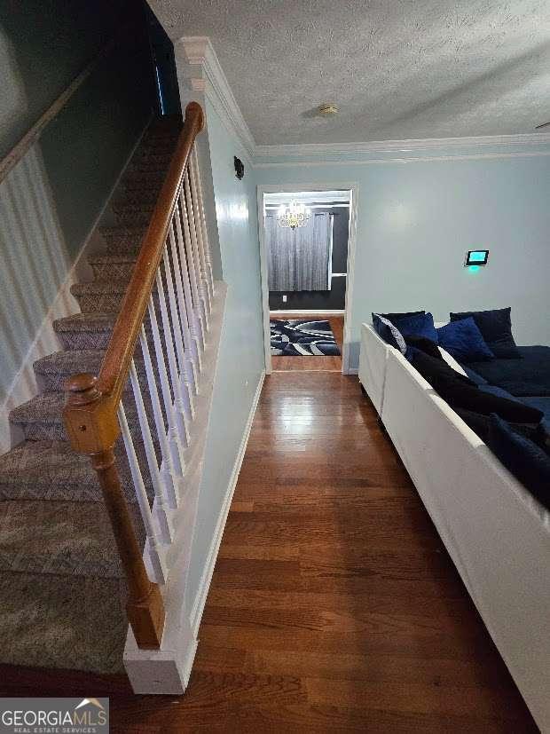 staircase featuring crown molding, hardwood / wood-style flooring, a textured ceiling, and a notable chandelier