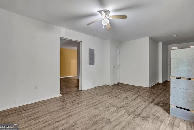 empty room with ceiling fan, electric panel, wood finished floors, and baseboards