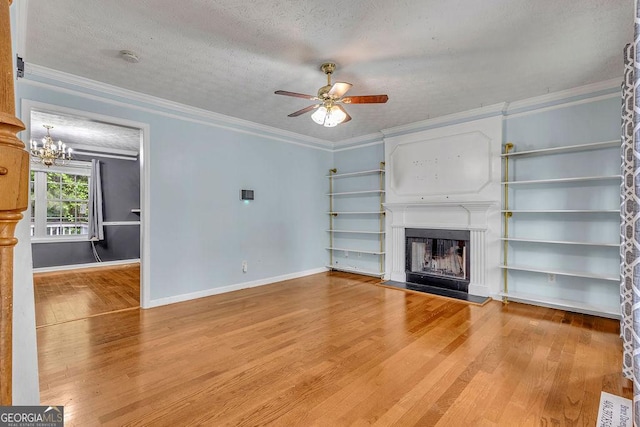 unfurnished living room featuring wood finished floors, ceiling fan, a fireplace, crown molding, and a chandelier