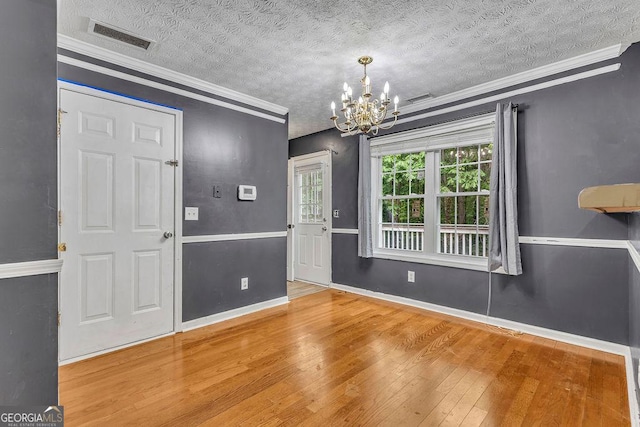 entryway with a chandelier, hardwood / wood-style flooring, a textured ceiling, baseboards, and crown molding