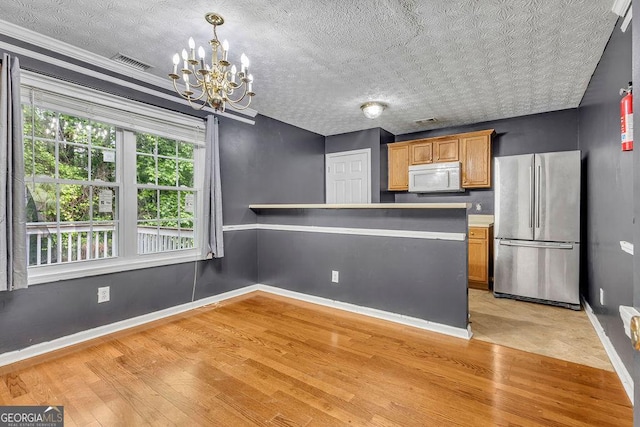 kitchen featuring freestanding refrigerator, white microwave, light wood-style flooring, a chandelier, and baseboards