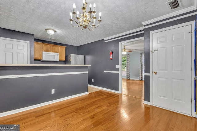 unfurnished dining area featuring light wood-style flooring, a chandelier, a textured ceiling, baseboards, and ornamental molding