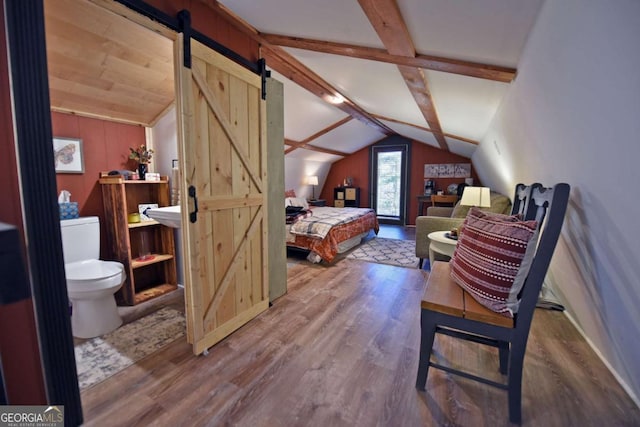 bedroom featuring hardwood / wood-style floors, vaulted ceiling with beams, and a barn door