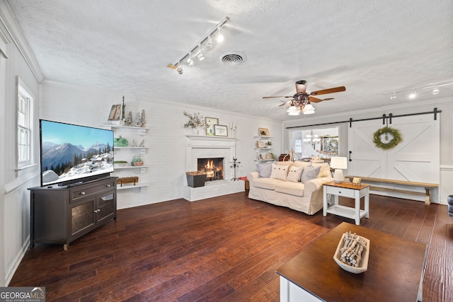 living room featuring ceiling fan, a barn door, dark hardwood / wood-style flooring, and a textured ceiling