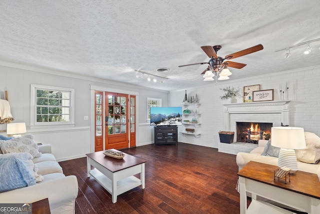 living room featuring ceiling fan, a brick fireplace, dark hardwood / wood-style flooring, a textured ceiling, and ornamental molding