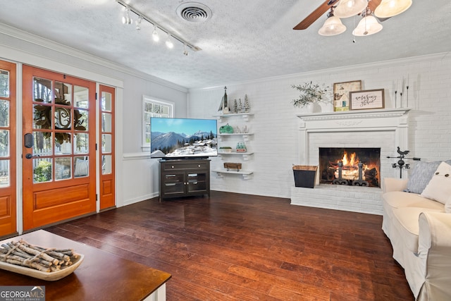 living room with dark hardwood / wood-style floors, ceiling fan, a textured ceiling, a fireplace, and brick wall