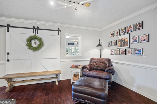 sitting room featuring a textured ceiling, a barn door, hardwood / wood-style flooring, and crown molding