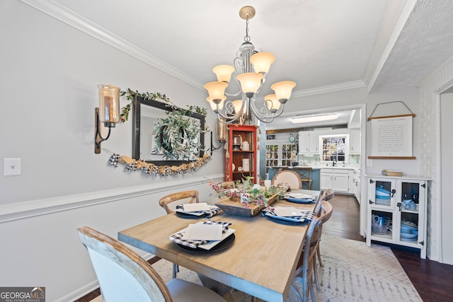 dining space with wood-type flooring, ornamental molding, sink, and an inviting chandelier