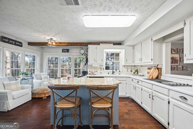 kitchen with tasteful backsplash, stainless steel gas cooktop, sink, white cabinets, and a breakfast bar area