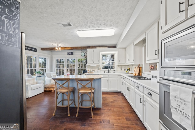 kitchen featuring white cabinets, a breakfast bar area, dark hardwood / wood-style floors, a textured ceiling, and stainless steel appliances