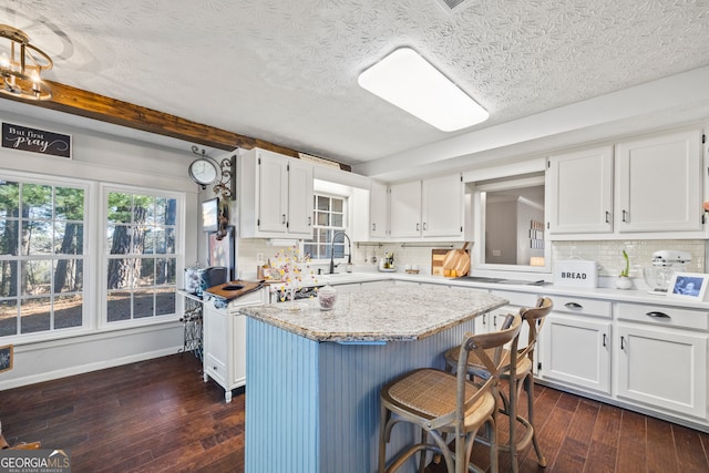 kitchen featuring backsplash, dark wood-type flooring, sink, white cabinets, and a kitchen island