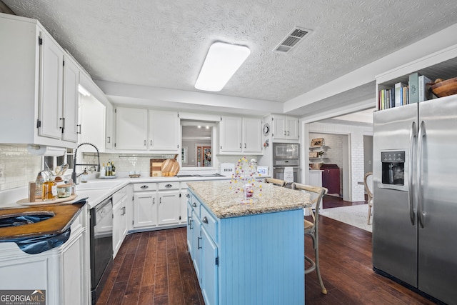 kitchen with a breakfast bar, stainless steel appliances, dark wood-type flooring, white cabinets, and a center island