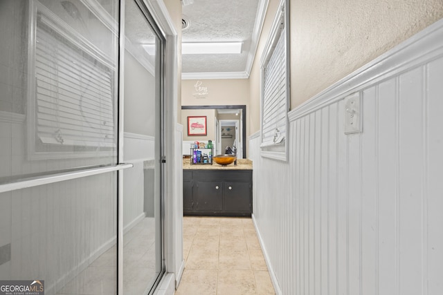 corridor with a textured ceiling, ornamental molding, and light tile patterned flooring