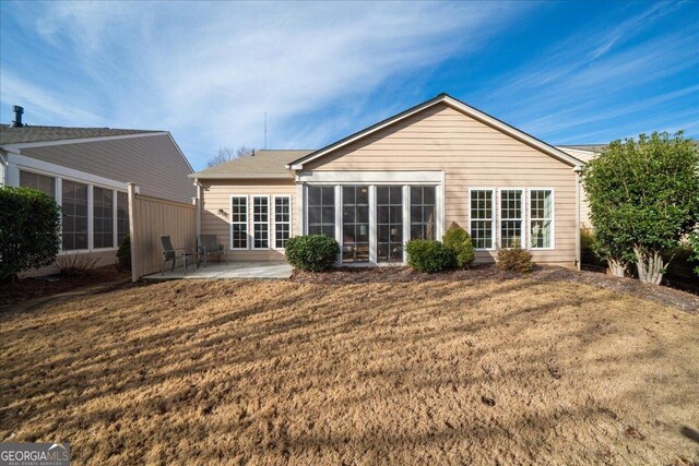 rear view of property featuring a sunroom, a patio area, and a lawn