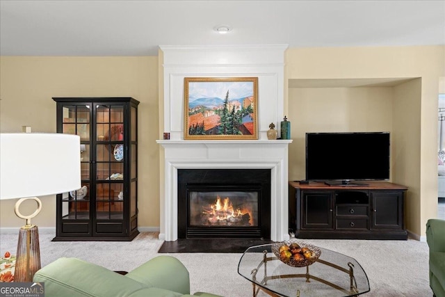 carpeted living area with a fireplace with flush hearth and baseboards