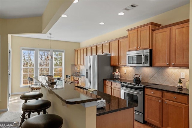 kitchen with backsplash, stainless steel appliances, decorative light fixtures, a center island with sink, and a notable chandelier