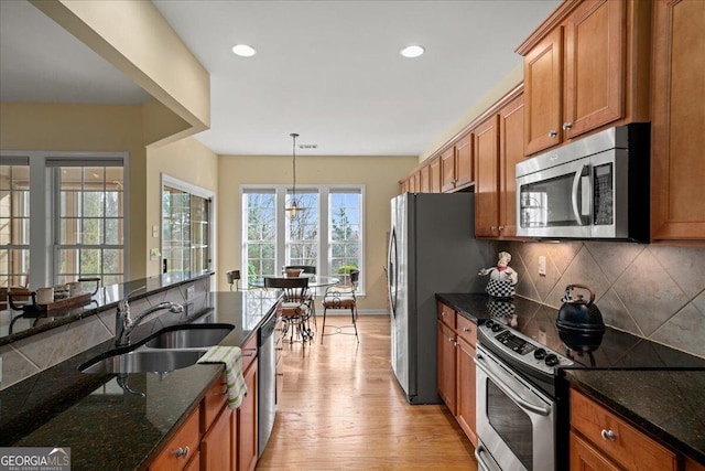 kitchen featuring light wood-style flooring, a sink, appliances with stainless steel finishes, tasteful backsplash, and brown cabinetry