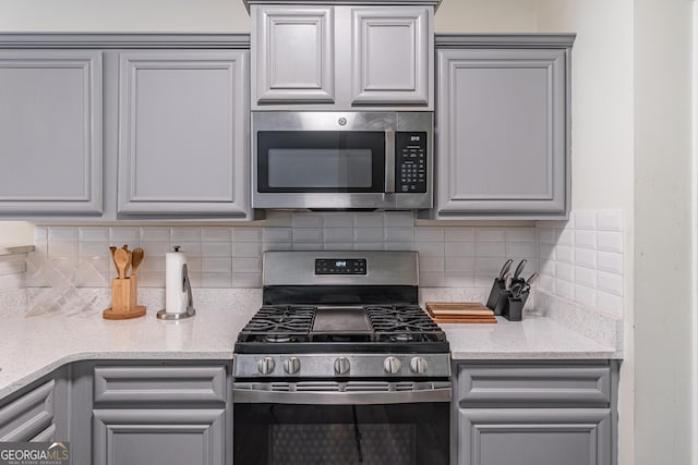 kitchen featuring backsplash, gray cabinetry, light stone countertops, and stainless steel appliances