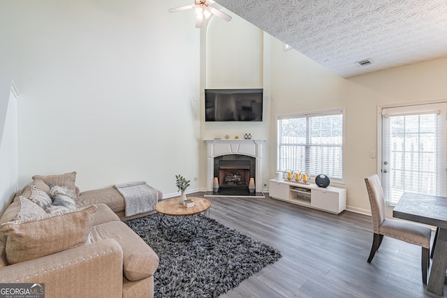 living room featuring ceiling fan, hardwood / wood-style floors, high vaulted ceiling, and a textured ceiling