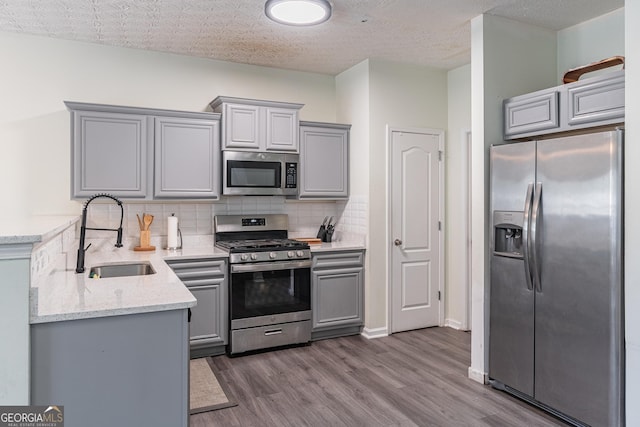 kitchen with light stone countertops, decorative backsplash, a textured ceiling, stainless steel appliances, and sink