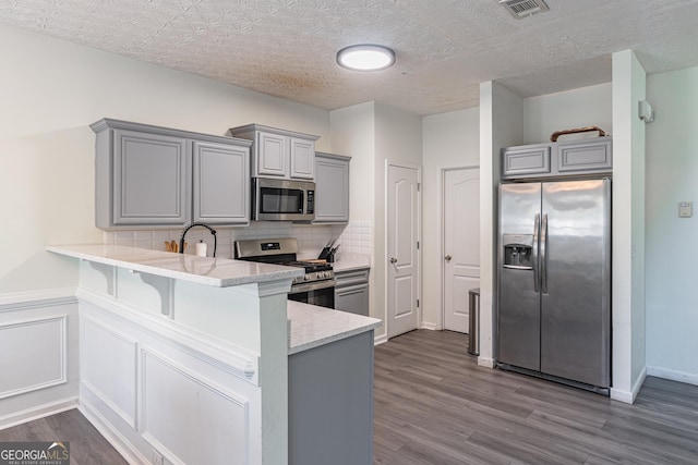 kitchen with kitchen peninsula, a kitchen breakfast bar, gray cabinetry, a textured ceiling, and stainless steel appliances