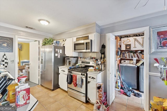 kitchen with appliances with stainless steel finishes, white cabinetry, washer and clothes dryer, and light tile patterned flooring