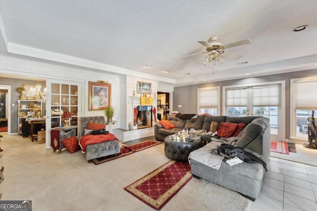 tiled living room with french doors, a textured ceiling, a tray ceiling, ceiling fan, and a fireplace