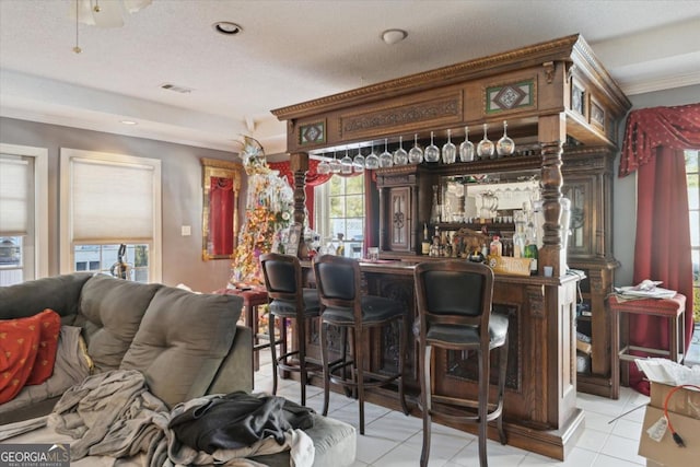 bar featuring light tile patterned flooring, a textured ceiling, and ornamental molding