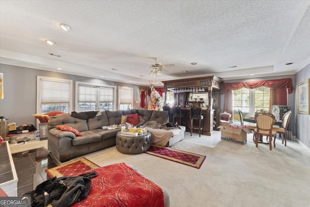 carpeted living room with ceiling fan, bar area, crown molding, a textured ceiling, and a tray ceiling