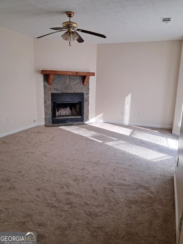 unfurnished living room featuring carpet, a textured ceiling, a stone fireplace, and ceiling fan