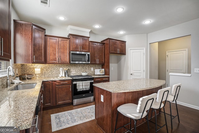 kitchen featuring stainless steel appliances, light stone countertops, a kitchen island, and sink