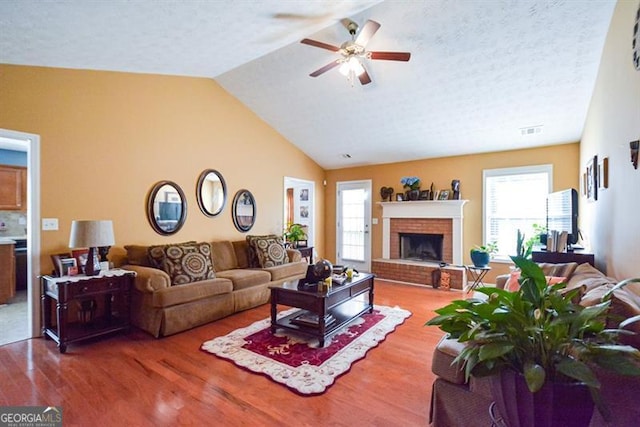 living room featuring a textured ceiling, hardwood / wood-style flooring, a brick fireplace, and lofted ceiling