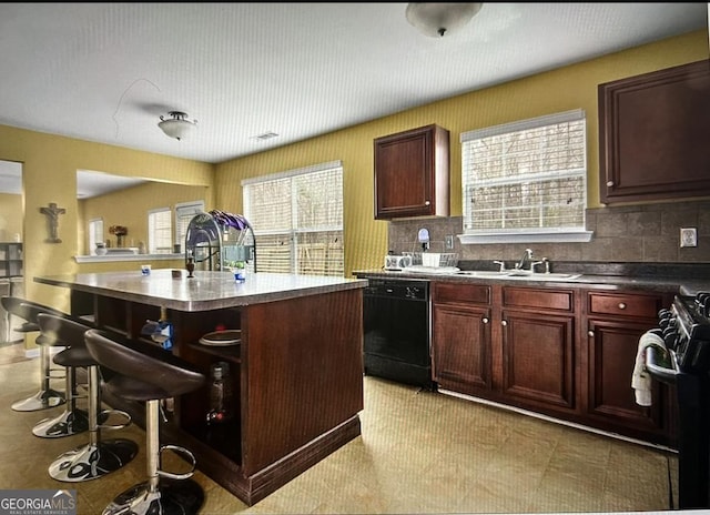 kitchen featuring a kitchen island with sink, black appliances, sink, decorative backsplash, and a healthy amount of sunlight