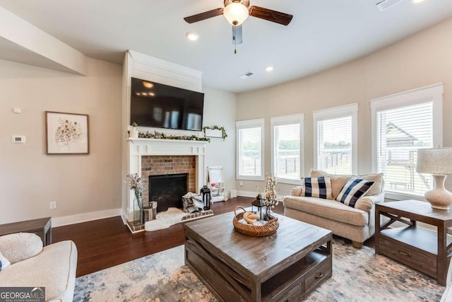 living room with hardwood / wood-style flooring, ceiling fan, and a brick fireplace