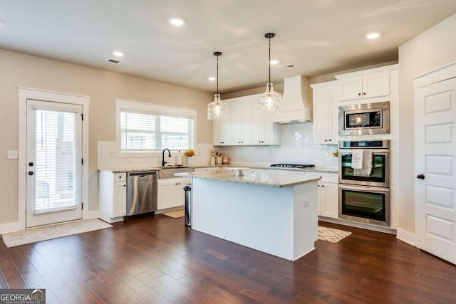 kitchen with appliances with stainless steel finishes, premium range hood, white cabinets, a center island, and hanging light fixtures