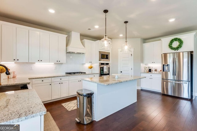 kitchen with custom exhaust hood, stainless steel appliances, sink, white cabinets, and a kitchen island